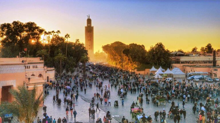 La place Jemaa el-Fnaa de Marrakech au coucher du soleil, foule animée et minaret de la mosquée Koutoubia se découpant sur un ciel doré