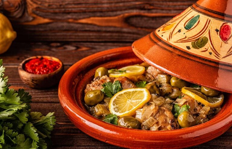 Tajine de poulet au citron confit, olives vertes et coriandre dans un plat en terre cuite conique décoré, avec harissa et coriandre fraîche