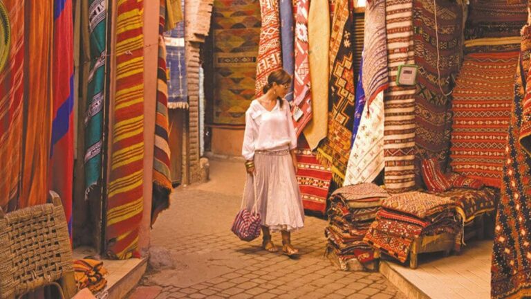 Visiteuse parcourant le Souk Zrabia de Marrakech, entourée de tapis berbères et de kilims colorés suspendus