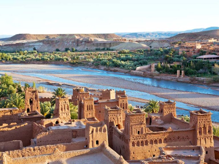 Vue aérienne du ksar d'Aït Benhaddou : tours en pisé rouge, palmiers et rivière Ounila serpentant dans la vallée