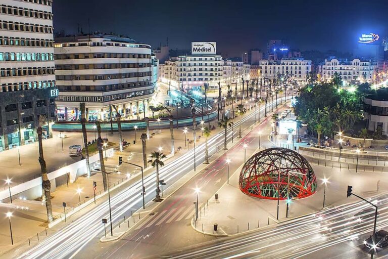 Vue nocturne du centre-ville de Casablanca, avenues illuminées, palmiers et sculpture en dôme sur une place animée