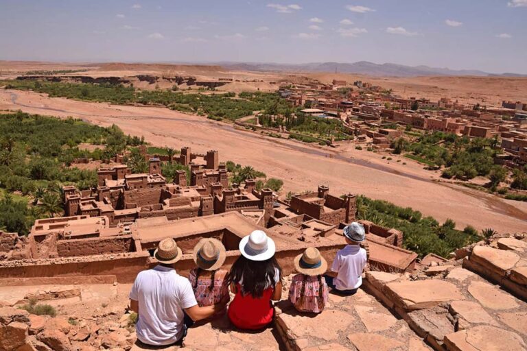 Famille en chapeaux de paille admirant la kasbah d'Aït Ben Haddou et la vallée depuis un belvédère lors d'une excursion depuis Marrakech