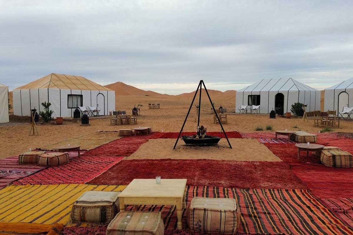 White ensuite tents, Berber rugs and a central fire pit at the Erg Chebbi luxury camp — your Day 2 overnight on the Marrakech to Casablanca route.