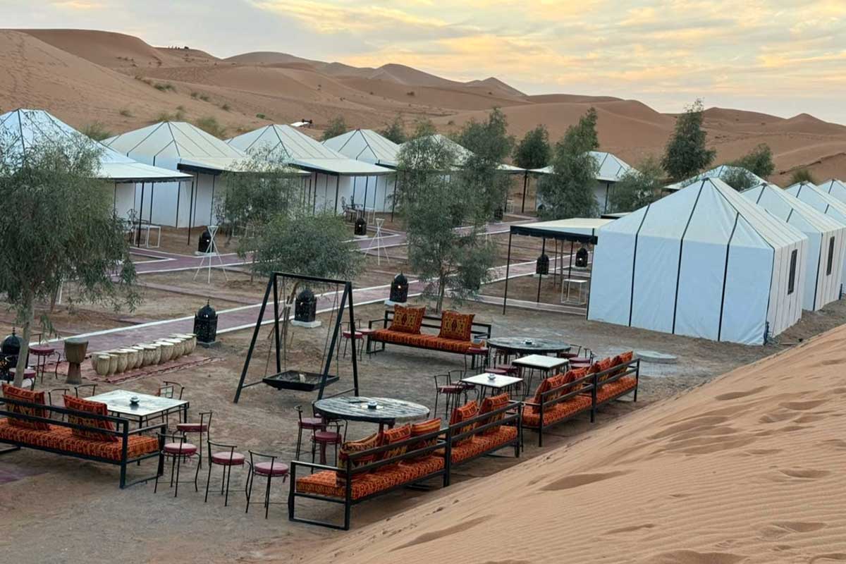 The deluxe Erg Chebbi camp at dusk — Berber lounge, lanterns and private tents set among the dunes.